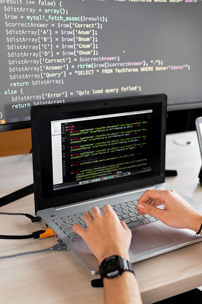 services-02 Person coding at a desk with laptop and external monitor showing programming code.